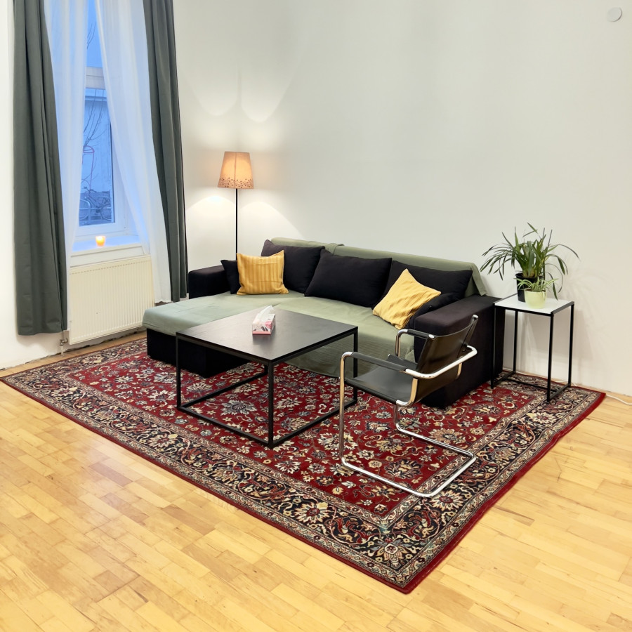 Praxisraum f&uuml;r Psychotherapie mit einem Sofa und Couchtisch und Sessel auf einem roten Teppich